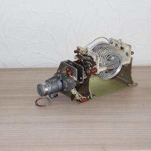 Peut inclure: Un composant d'émetteur radio vintage comprenant une grande bobine d'induction argentée, un petit moteur cylindrique et divers câblages électriques montés sur une plaque de base métallique rectangulaire avec des pièces mécaniques exposées.