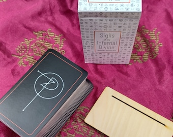 May include: A deck of cards with black backs and a white sigil on each card. The box is white with black text that reads "Sigils of the Infernal Divine Devotional & Divination Deck".