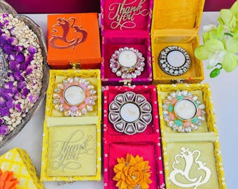 May include: Assortment of small, decorative boxes with lids. Each box features a different design, including a floral motif, a 'Thank You' inscription, and a religious symbol. The boxes are made of wood and have a colorful, patterned exterior.