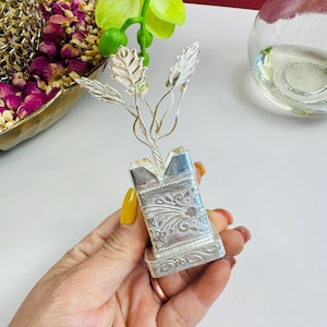 May include: A silver plant sculpture with a detailed, ornate base. The plant has three leaves and a twisted stem.