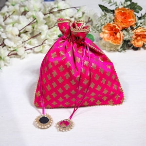 May include: A pink drawstring bag with a gold leaf pattern and gold trim. The bag has two small round mirrors with pearl accents attached to the drawstrings.
