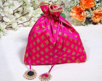 May include: A pink drawstring bag with a gold leaf pattern and gold trim. The bag has two small round mirrors with pearl accents attached to the drawstrings.