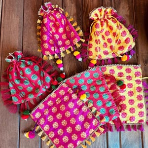 K&ouml;nnte beinhalten: F&uuml;nf bunte Stoffbeutel mit Quasten und Bommeln. Die Beutel sind mit floralen Mustern in Rosa-, Gelb- und Gr&uuml;nt&ouml;nen verziert.