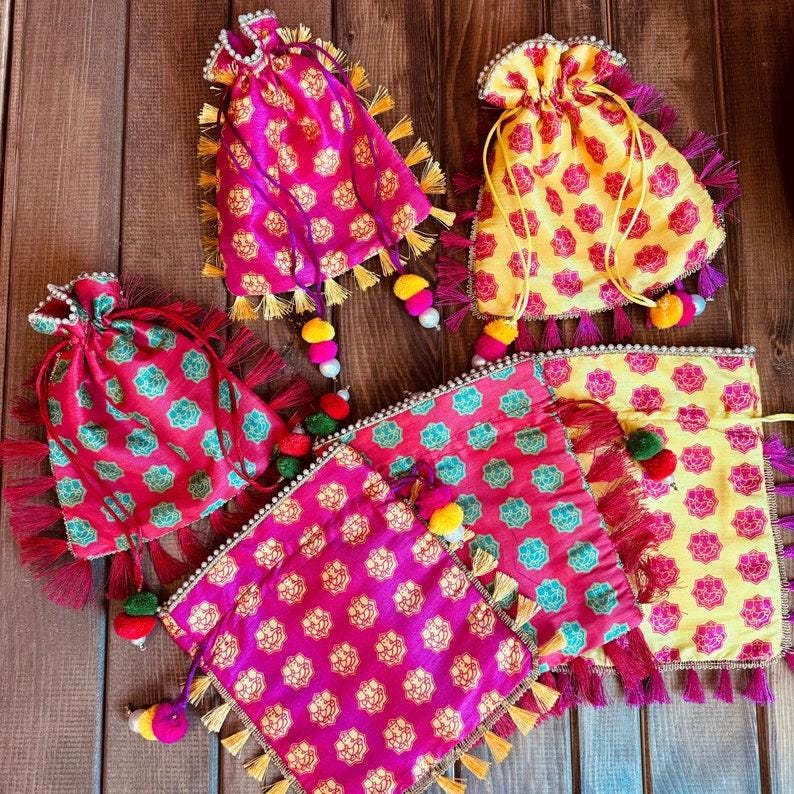 K&ouml;nnte beinhalten: F&uuml;nf bunte Stoffbeutel mit Quasten und Bommeln. Die Beutel sind mit floralen Mustern in Rosa-, Gelb- und Gr&uuml;nt&ouml;nen verziert.