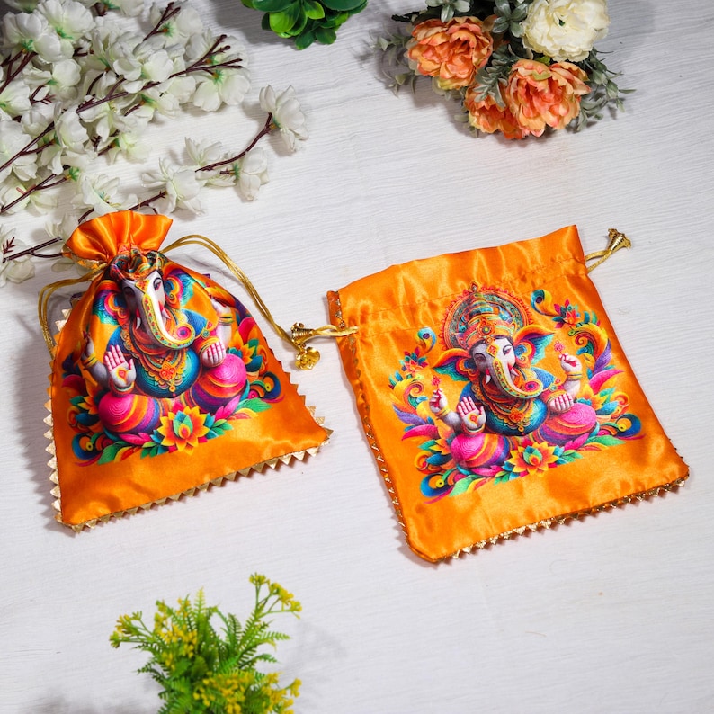 K&ouml;nnte beinhalten: Zwei orangefarbene Satin-Zugbeutel mit goldenen Verzierungen. Jeder Beutel zeigt eine farbenfrohe Illustration der hinduistischen Gottheit Ganesha.