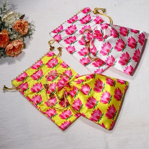 K&ouml;nnte beinhalten: Zwei Kordelbeutel mit rosa Lotusblumenmustern. Ein Beutel ist wei&szlig; mit rosa Blumen und der andere ist gelb mit rosa Blumen.