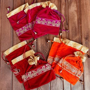 May include: Set of six small drawstring bags with gold trim and embroidered designs. The bags are made of velvet and come in two colors: red and orange.