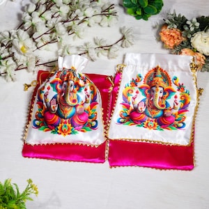 K&ouml;nnte beinhalten: Zwei wei&szlig;e Satin-Zugbeutel mit rosa Satinbesatz und goldenen Akzenten. Jeder Beutel zeigt eine farbenfrohe Illustration der hinduistischen Gottheit Ganesha.