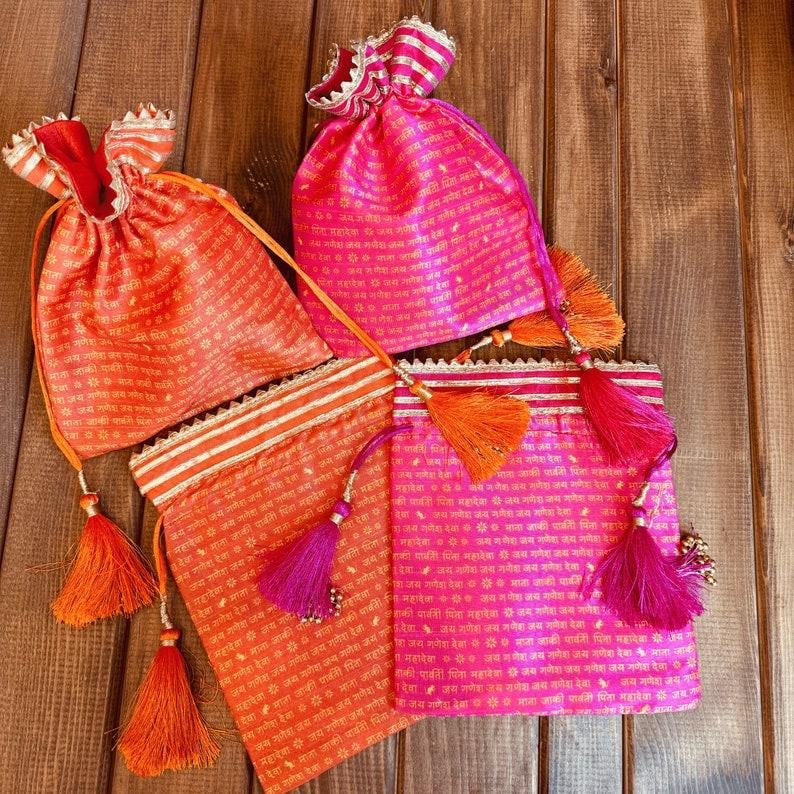 K&ouml;nnte beinhalten: Vier kleine Kordelbeutel mit Quasten. Die Beutel sind aus rosa und orangefarbenem Stoff mit goldenen Verzierungen und mit gedrucktem Text verziert.