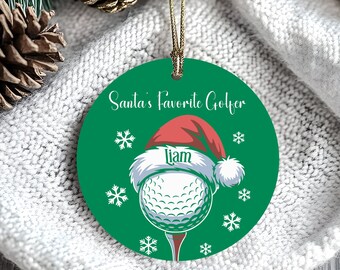 Puede incluir: Un adorno navideño verde con el texto "Santa's Favorite Golfer" y copos de nieve. El adorno presenta una pelota de golf con un gorro de Papá Noel con el nombre "Liam". El adorno cuelga de una cuerda dorada.