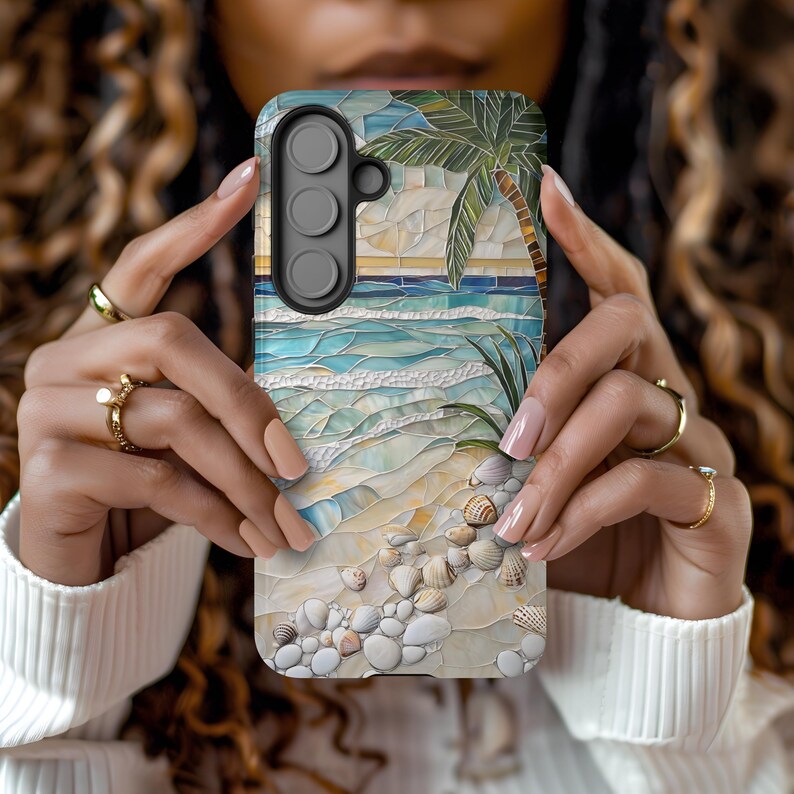 May include: A phone case featuring a mosaic design of a beach scene with a palm tree, ocean waves, and seashells. The case has a black camera module and is held by a person.