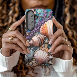 May include: A phone case with a mosaic design featuring seashells, pearls, and rhinestones. The case has a blue, green, and purple color scheme.