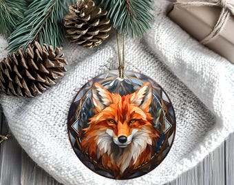 May include: Round Christmas ornament featuring a detailed illustration of a fox with orange and white fur, set against a geometric background. The ornament has a gold string for hanging and is a festive holiday decoration.