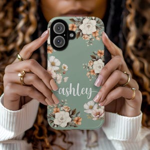 May include: A sage green phone case with a floral design and the name "ashley" printed on it.