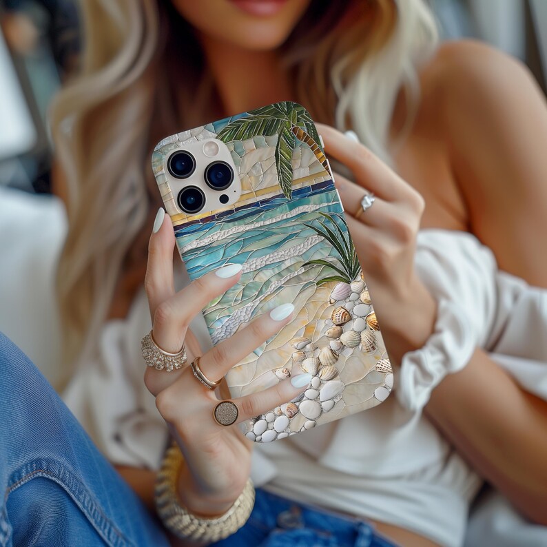 May include: A phone case featuring a beach scene with a palm tree, ocean waves, and seashells. The case has a mosaic-like design with shades of blue, beige, and green. The phone case is held by a person.