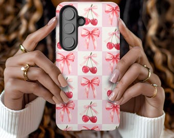 May include: A pink and white phone case with a repeating pattern of cherries and pink bows.