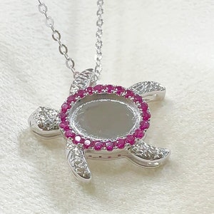 May include: Silver turtle pendant necklace with a round bezel set with pink gemstones. The pendant is on a silver chain.