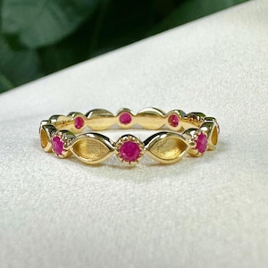May include: A gold ring featuring a repeating pattern of small, round, bright red gemstones. The ring's band has an openwork design with a series of oval and floral shapes. The ring is set against a white background.