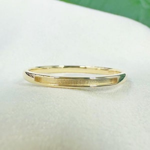 May include: A gold ring featuring a rectangular textured detail. The band is a simple design with a polished exterior and a recessed, textured centre. The ring is displayed against a soft, white backdrop.
