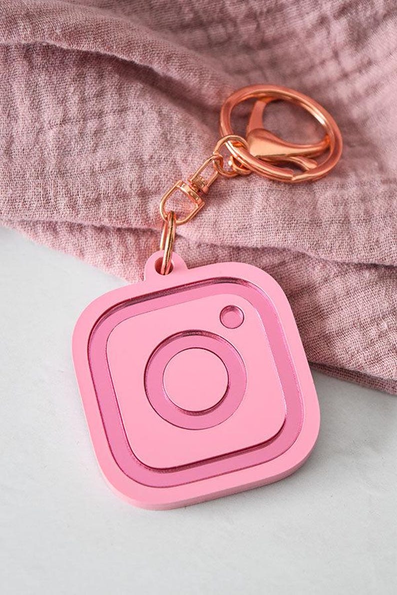 以下が含まれることがあります： ピンクのInstagramロゴのキーホルダーで、ローズゴールドのキーリングが付いています。