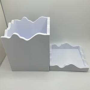 May include: A white, two-piece storage container with a mountain-like edge design. The larger piece is a box, and the smaller piece is a tray. The container is made of a solid, opaque material.