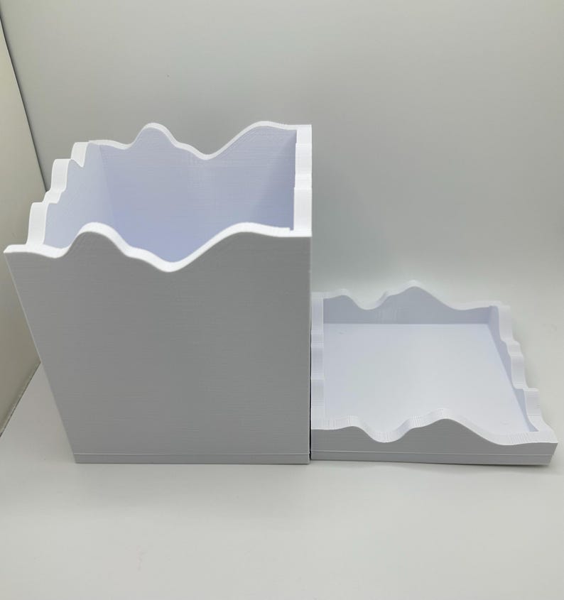 May include: A white, two-piece storage container with a mountain-like edge design. The larger piece is a box, and the smaller piece is a tray. The container is made of a solid, opaque material.