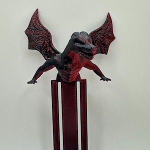 May include: A red and black dragon figurine with wings outstretched, perched on a red, textured, rectangular base.