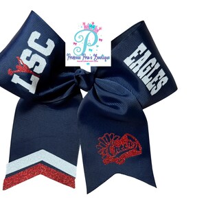 May include: A navy blue cheer bow made of grosgrain ribbon. The left loop features white text LSC with a red glitter accent, while the right loop displays white text EAGLES. One tail has red and white glitter chevrons, the other a red glitter graphic.