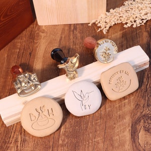 May include: Five different metal stamps for pottery, featuring designs of a hummingbird, a plant, a coffee cup, and two different leaf designs. The stamps are arranged on a wooden surface.