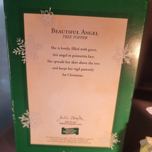 May include: A porcelain angel tree topper with a white dress and poinsettia lace. The angel is holding a white star and has a gold halo. The box features the text "Beautiful Angel Tree Topper" and a poem about the angel. The box is green with snowflakes.