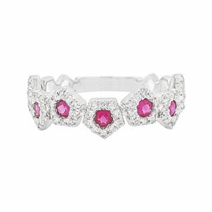 Puede incluir: Un anillo de plata con cinco engastes pentagonales. Cada engaste presenta una piedra central redonda de color rub&iacute;, rodeada de piedras claras m&aacute;s peque&ntilde;as. El dise&ntilde;o del anillo presenta un patr&oacute;n repetitivo.