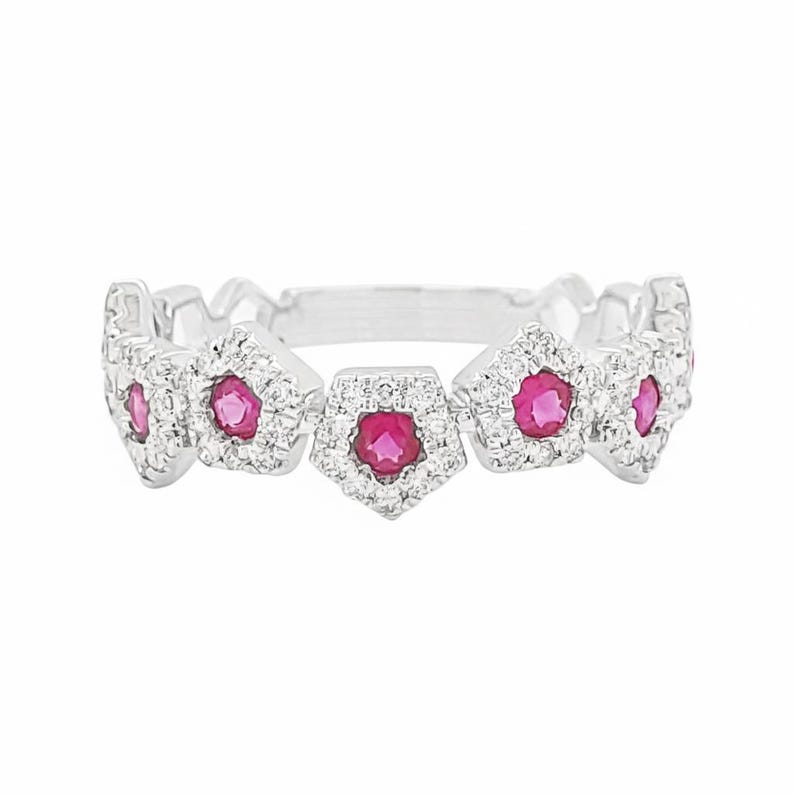 Puede incluir: Un anillo de plata con cinco engastes pentagonales. Cada engaste presenta una piedra central redonda de color rub&iacute;, rodeada de piedras claras m&aacute;s peque&ntilde;as. El dise&ntilde;o del anillo presenta un patr&oacute;n repetitivo.