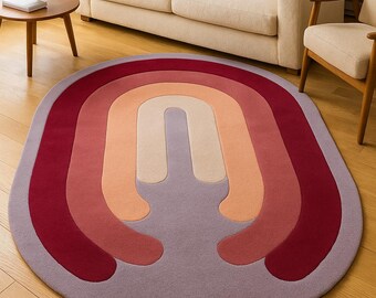 May include: An oval-shaped rug with a rainbow design. The rug features a series of curved bands in shades of red, orange, and purple. The rug is placed on a hardwood floor, and the overall aesthetic is modern and inviting.