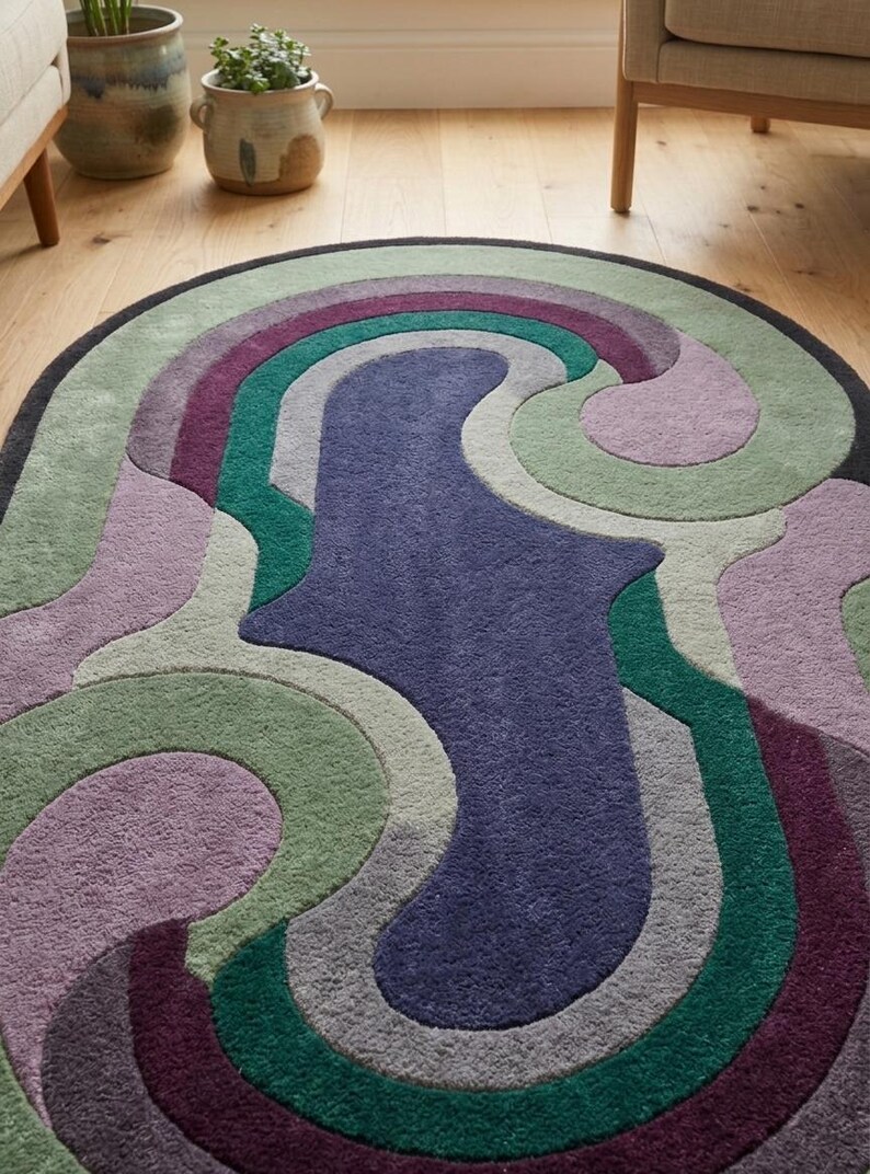 Puede incluir: Alfombra ovalada con un dise&ntilde;o abstracto y colorido. La alfombra presenta una forma central azul oscuro rodeada de patrones arremolinados en tonos de morado, verde y gris. La alfombra est&aacute; sobre un suelo de madera.