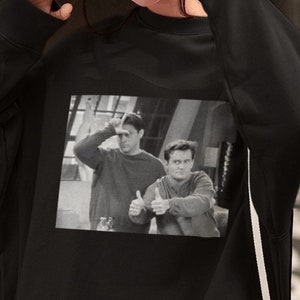 Op de afbeelding: Zwart sweatshirt met een grafische print van twee mannen uit de tv-serie Friends. De mannen geven een duim omhoog.