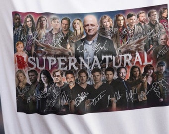 May include: White t-shirt featuring a graphic of the cast of the television show "Supernatural" with their signatures. The graphic includes the show's title in large letters. The shirt is made of a soft, comfortable material.