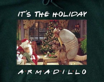 May include: Forest green hoodie with a Christmas-themed graphic featuring a cartoon armadillo and Santa Claus. The text "It's the Holiday Armadillo" is printed on the hoodie.