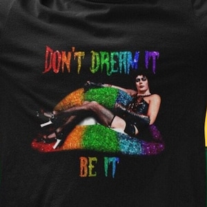 May include: Black t-shirt with a rainbow glitter lips design and the text "Don't Dream It, Be It".