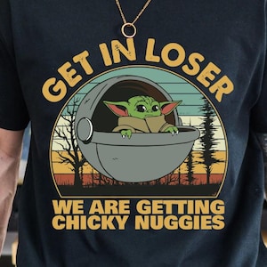 May include: Black t-shirt featuring a graphic of Grogu in a pod with the text "GET IN LOSER WE ARE GETTING CHICKY NUGGIES" in yellow and white. The design includes a sunset and trees.