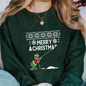 May include: A forest green sweatshirt with a white design featuring a cartoon character fishing. The design includes the text "Merry Christmas".