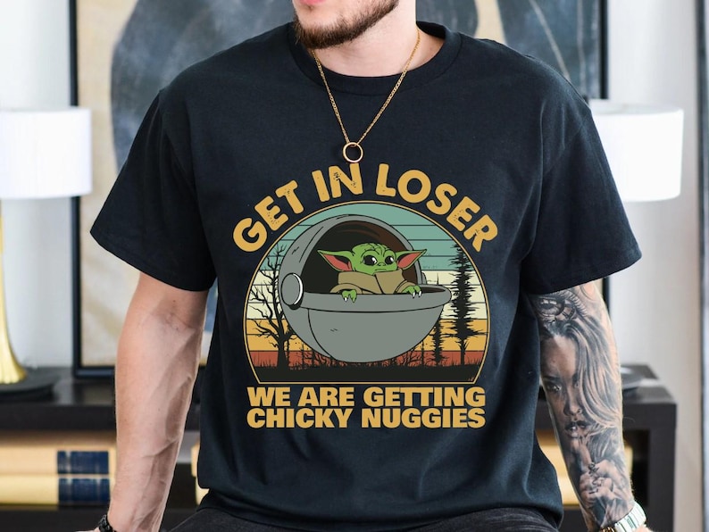May include: Black t-shirt featuring a graphic of Grogu in a pod with the text "GET IN LOSER WE ARE GETTING CHICKY NUGGIES" in yellow and white. The design includes a sunset and trees.