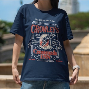 Pode incluir: Camiseta azul marinho com um design gr&aacute;fico em estilo vintage. O gr&aacute;fico diz "Crowley's Crossroads Inn" com texto incluindo "Fine Whiskey", "Great Deals" e "Cool Music". O design apresenta uma ilustra&ccedil;&atilde;o de touro.