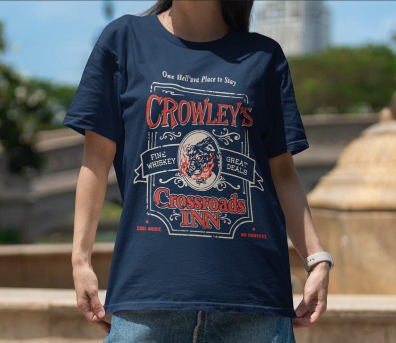 Pode incluir: Camiseta azul marinho com um design gr&aacute;fico em estilo vintage. O gr&aacute;fico diz "Crowley's Crossroads Inn" com texto incluindo "Fine Whiskey", "Great Deals" e "Cool Music". O design apresenta uma ilustra&ccedil;&atilde;o de touro.