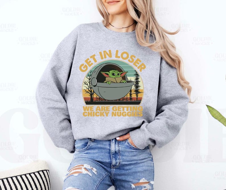 May include: A light gray sweatshirt with a graphic featuring a green alien character in a pod, with the text "GET IN LOSER" and "WE ARE GETTING CHICKY NUGGS". The design has a retro sunset and forest background.