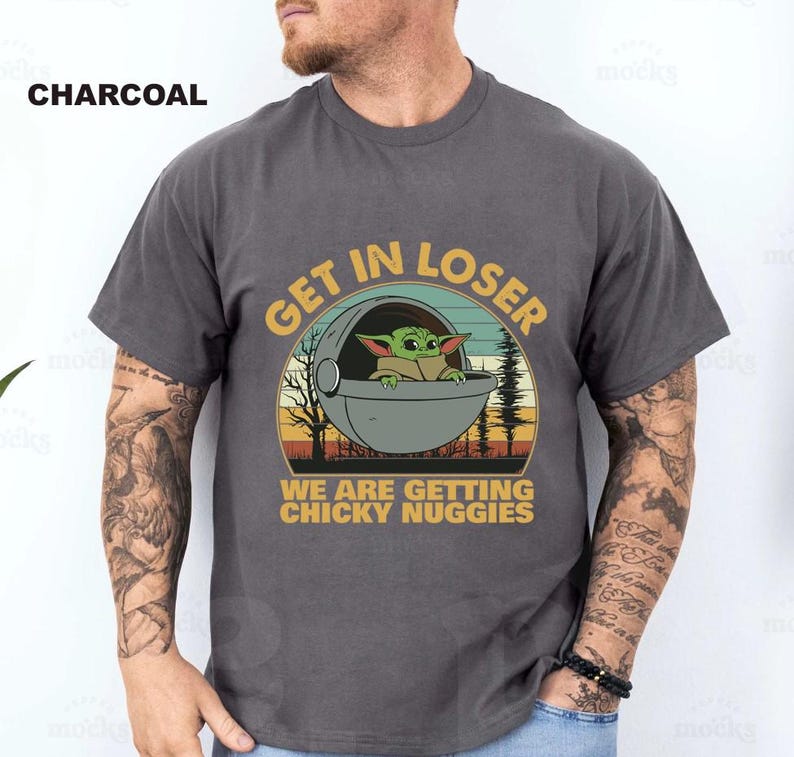 May include: Charcoal gray t-shirt featuring a graphic of Grogu in a pod with the text "GET IN LOSER WE ARE GETTING CHICKY NUGGIES" in a circular design. The design includes a sunset and trees.