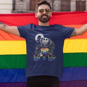 May include: A person wearing a navy blue t-shirt with a rainbow heart and the text "Love is Love" and a black and white illustration of Jack Skellington from The Nightmare Before Christmas. The person is holding a rainbow pride flag.