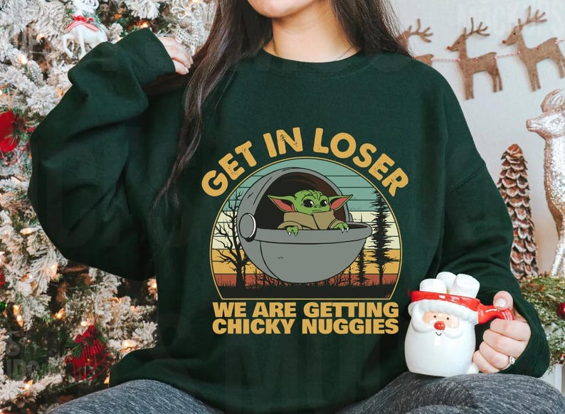 May include: Dark green sweatshirt with the text "GET IN LOSER" above a graphic of Baby Yoda in a pod. Below the graphic, the text reads "WE ARE GETTING CHICKY NUGGIES". The sweatshirt is a long-sleeved crew neck.
