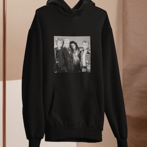 Op de afbeelding: Zwarte hoodie met een zwart-witfoto van een band. De bandleden dragen leren jacks en hebben lang haar.