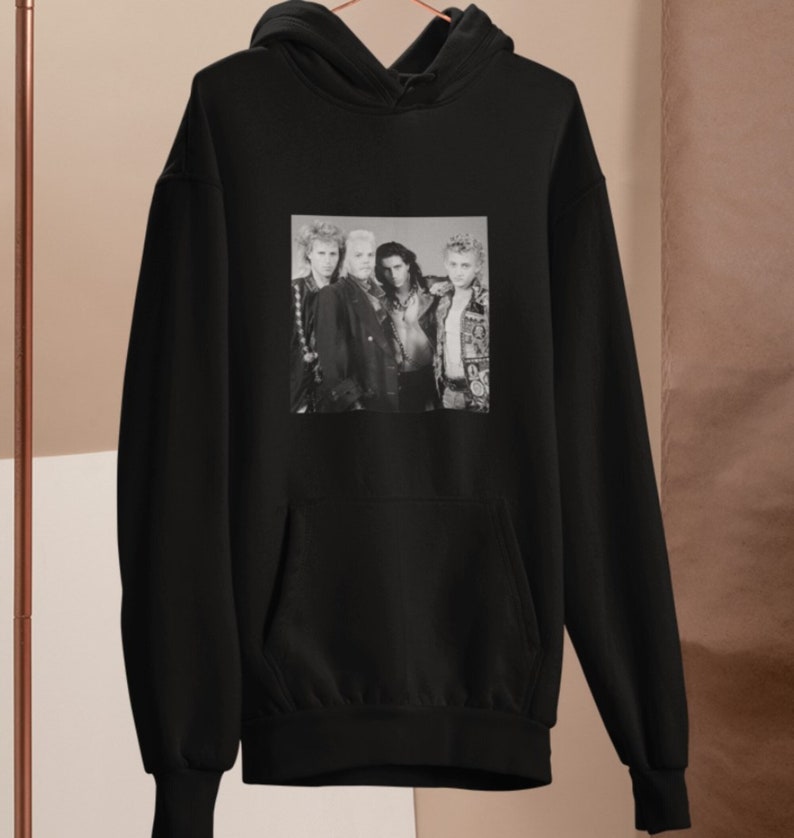 Op de afbeelding: Zwarte hoodie met een zwart-witfoto van een band. De bandleden dragen leren jacks en hebben lang haar.