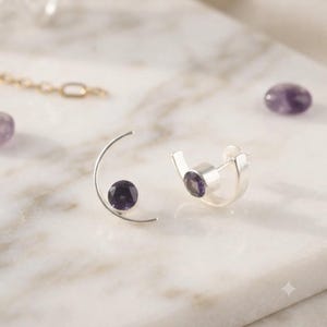 Peut inclure: Une paire de boucles d'oreilles en argent avec une monture métallique incurvée en forme de croissant et une pierre précieuse violette ronde et facettée au centre. Les boucles d'oreilles ont une fermeture à tige et une finition polie.